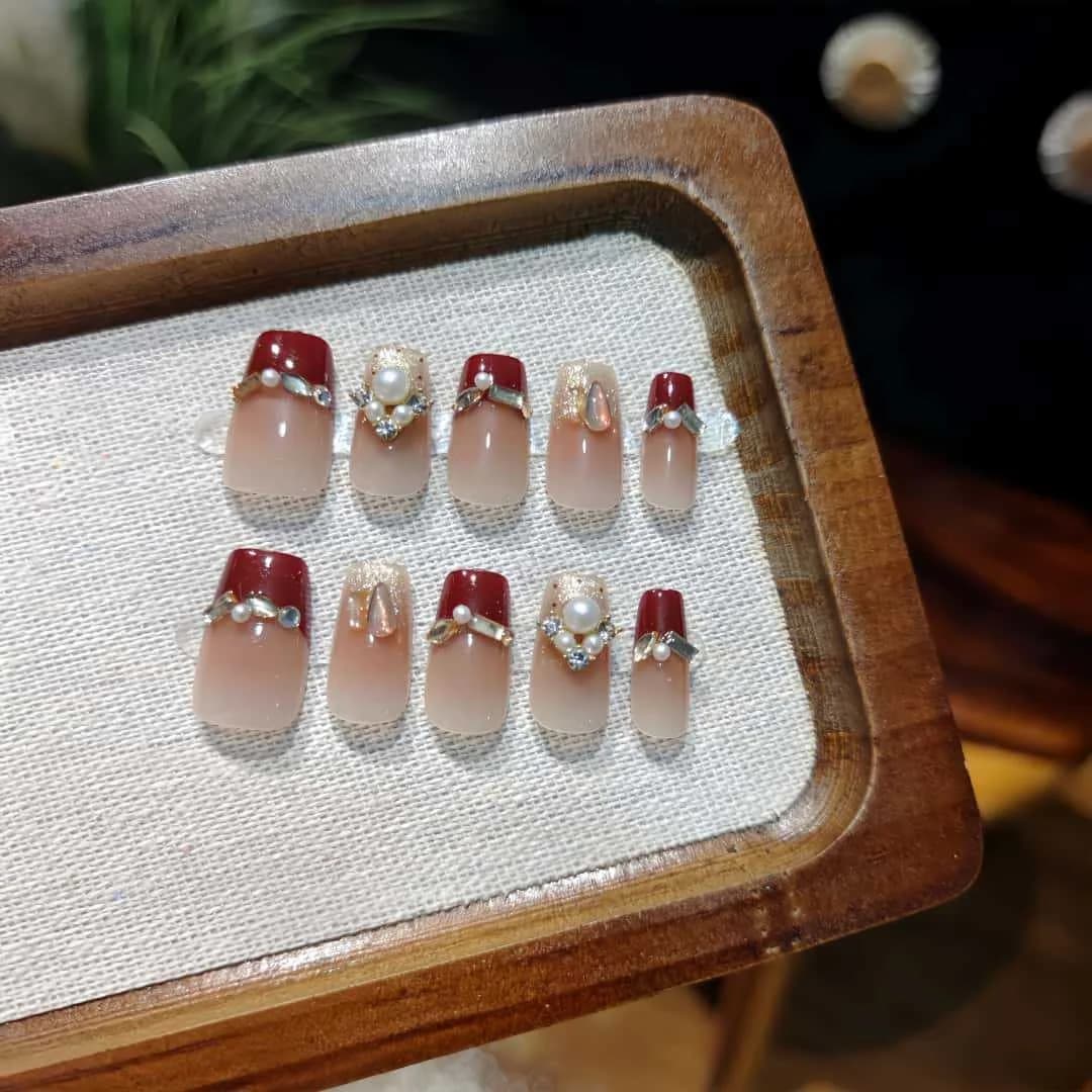 Czerwone perłowe paznokcie nakładane, krótkie coffin, francuski manicure z brokatem